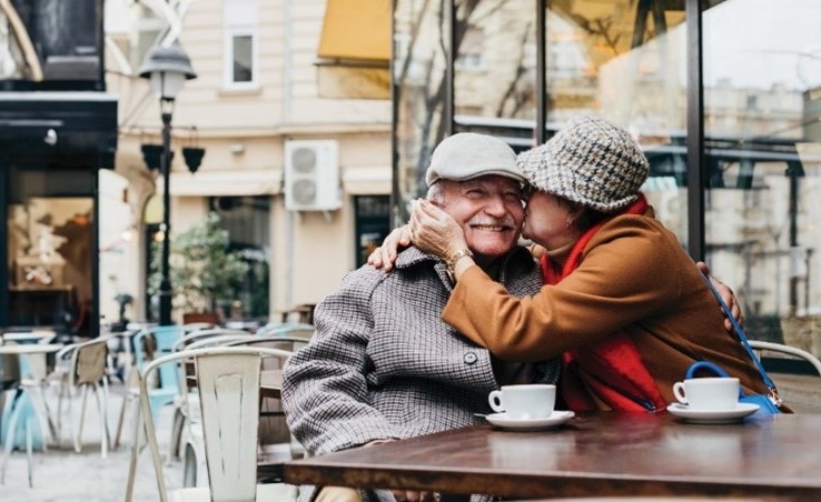 Woman warmly embraces man while they sit together at an outdoor cafe patio