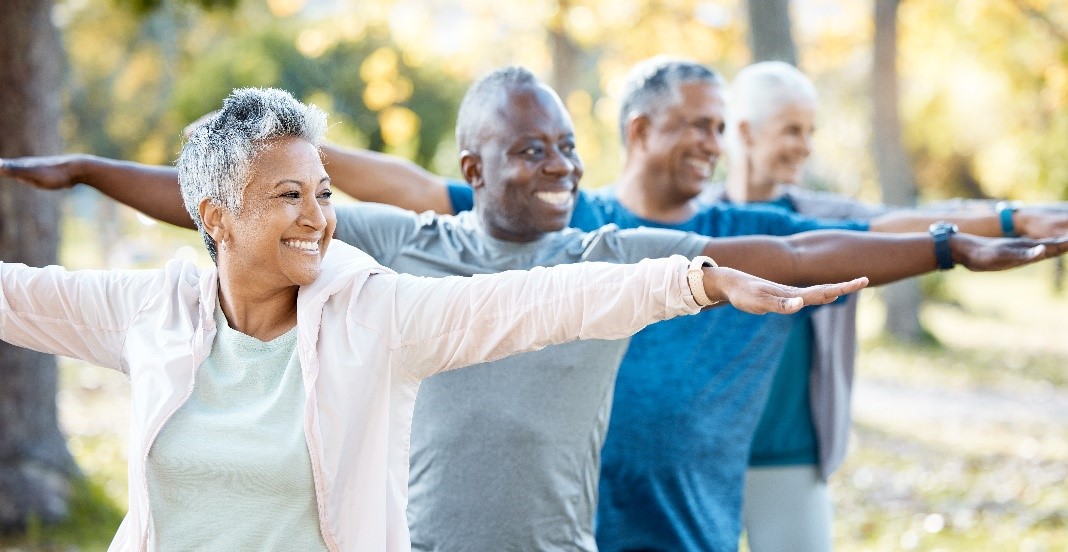 A smiling group of adults practice yoga outdoors