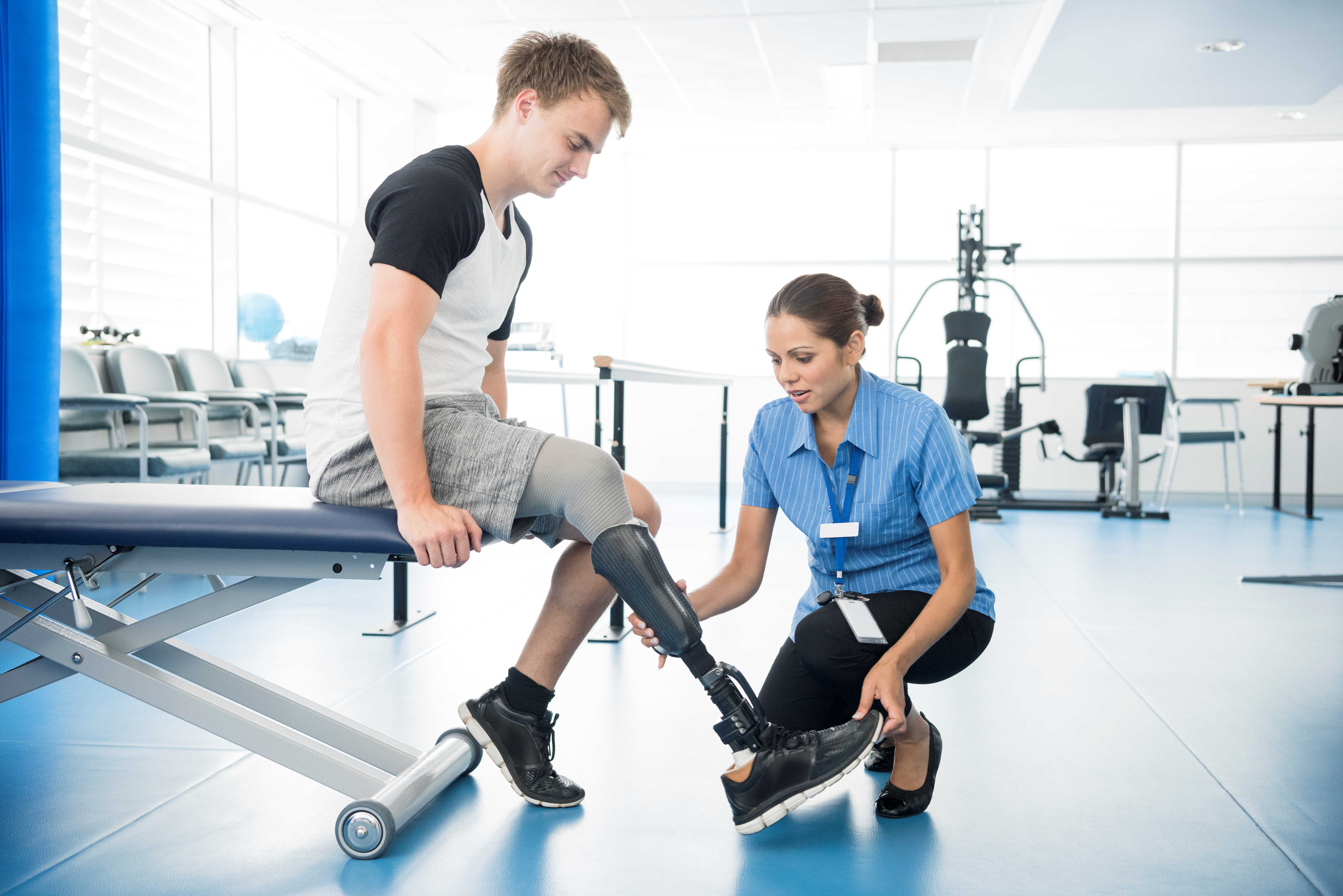 A nurse inspects a man's prostetic leg as he sits on a workout bench at a physical therapy facility.