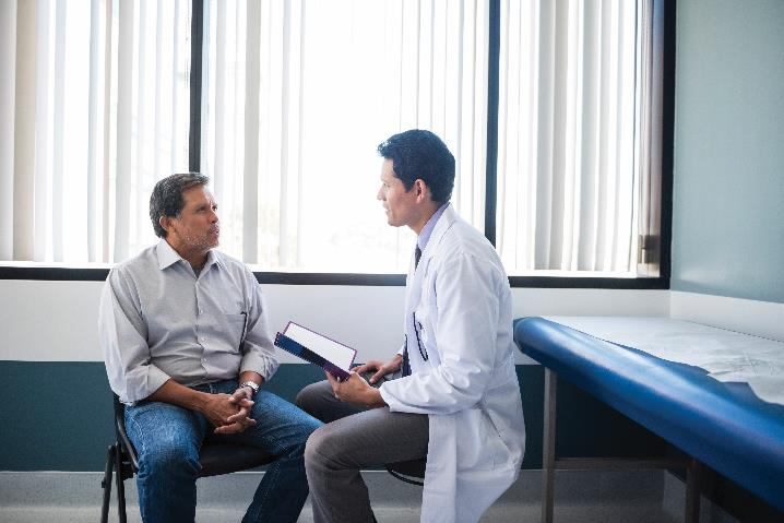 Image of male patient and male doctor speaking in an exam room.