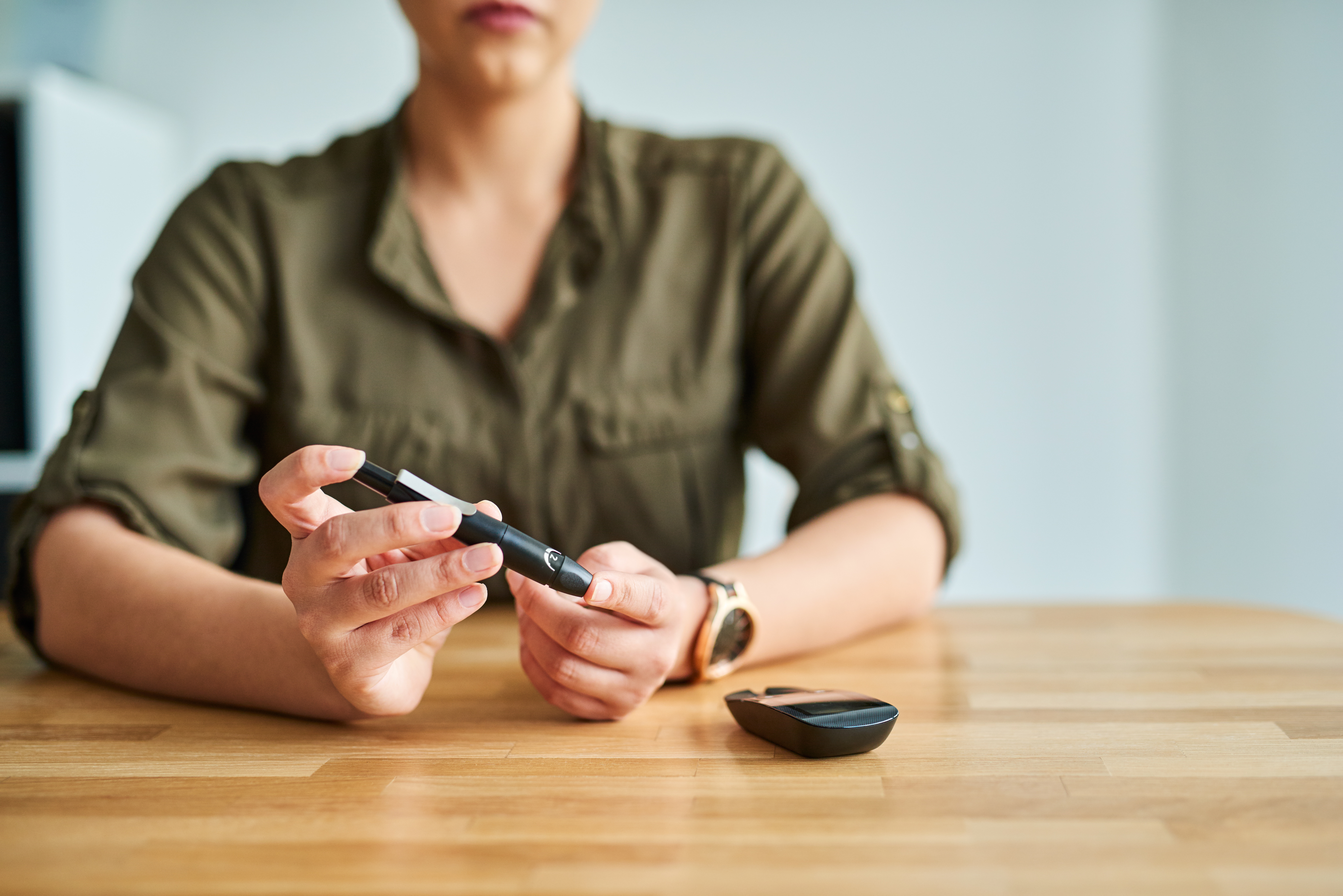 Woman sitting with diabetes equipment in hand and on table before her.