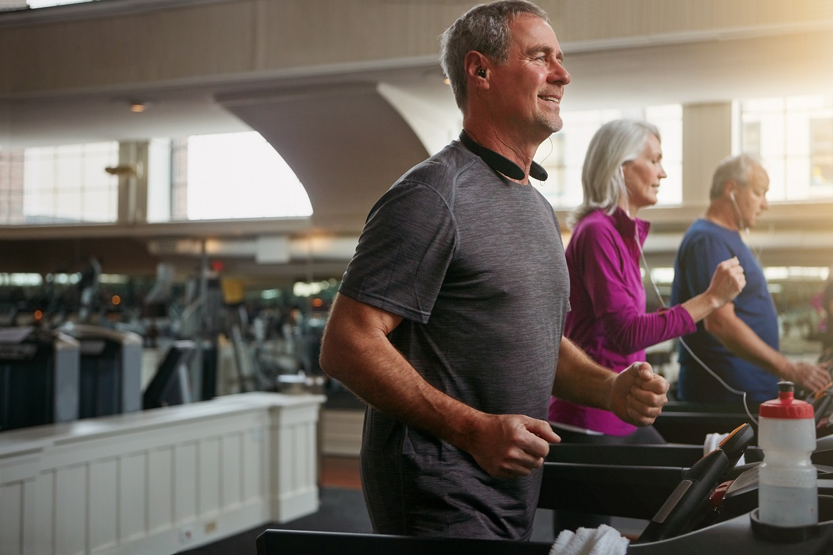 White-haired man on treadmill in a workout class with other retirees