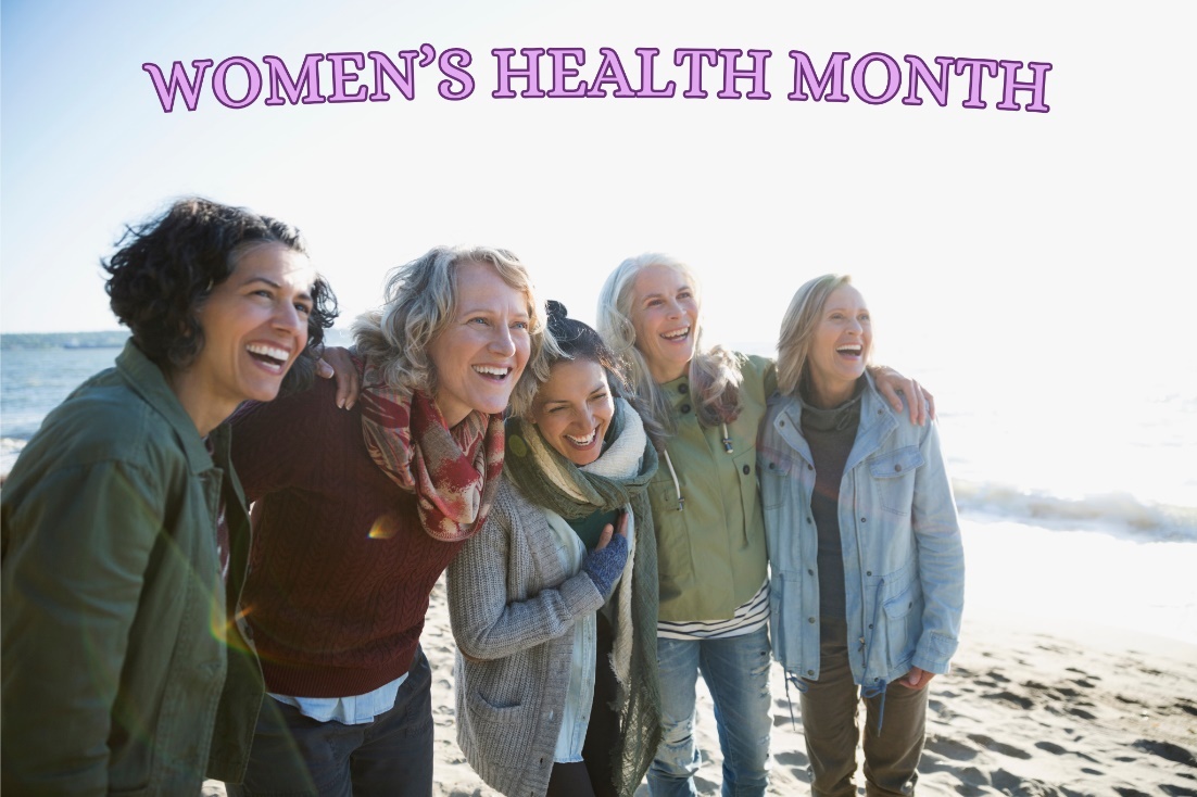 Banner reading “Women’s Health Month” above five adults standing close together with arms around one another on a sandy beach near the ocean in bright daylight.