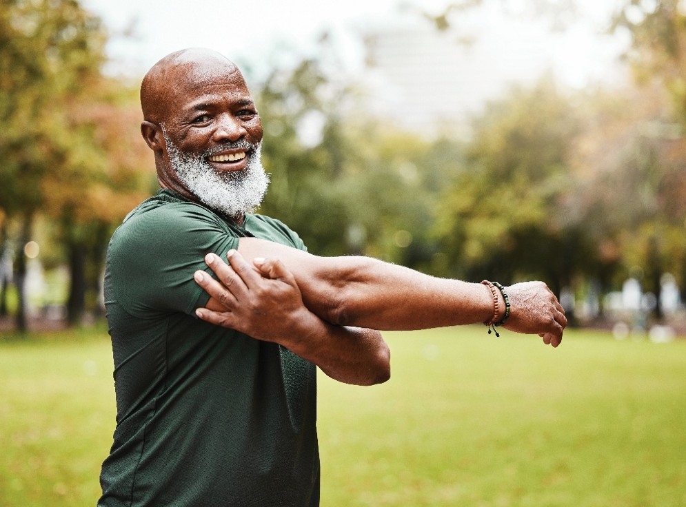 Man stretching an arm across the chest while exercising outdoors in a park.